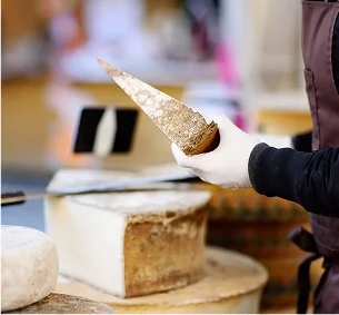 Personne gantée coupant un morceau de fromage à pâte dure dans un magasin à Pernes-les-Fontaines dans le Vaucluse 84